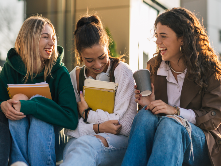 three students holding textbooks and laughing outside