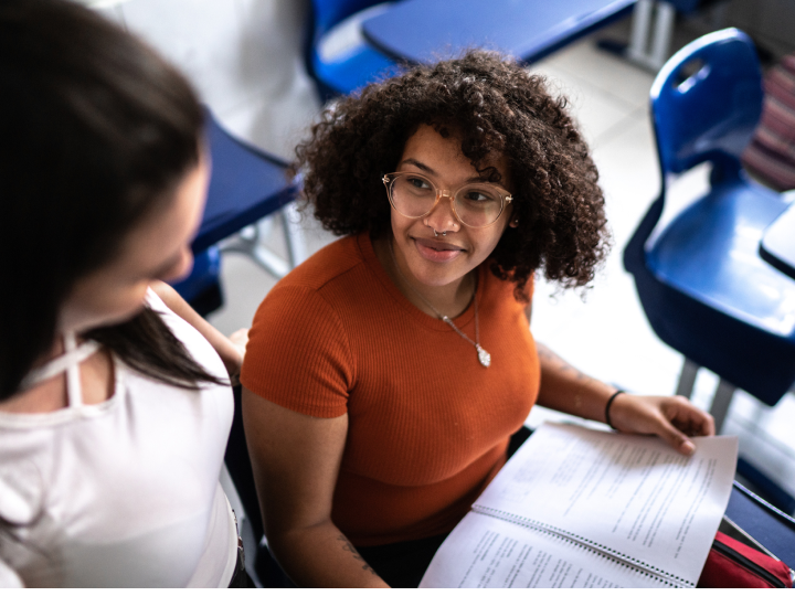 Student doing work at a school desk looking up at a friend