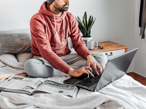 student studying using his laptop and textbooks on his bed