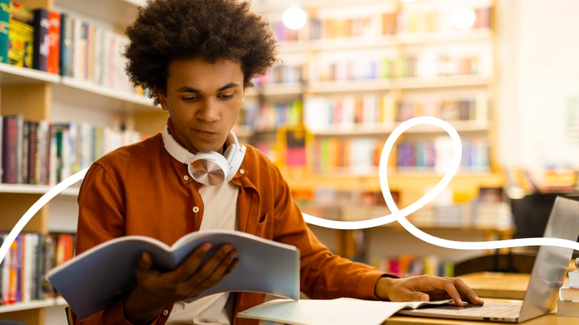 College student studying scholarship essay materials in a library while researching financial aid opportunities.