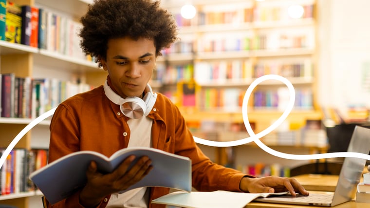 College student studying scholarship essay materials in a library while researching financial aid opportunities.