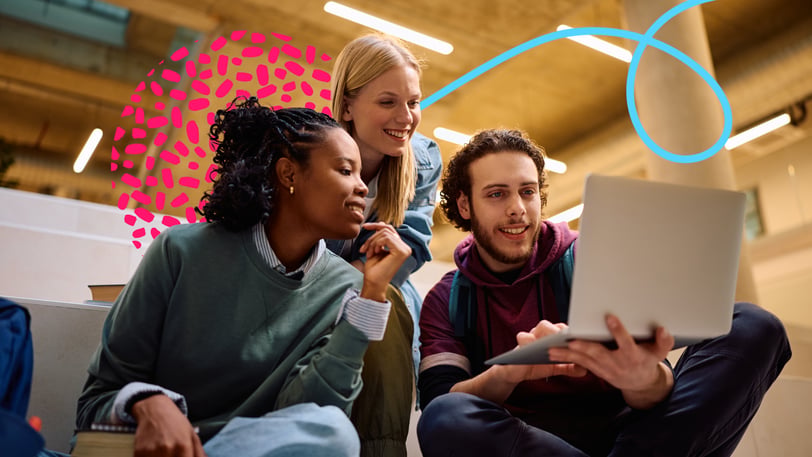 Three college students smiling and looking at a laptop together on campus.